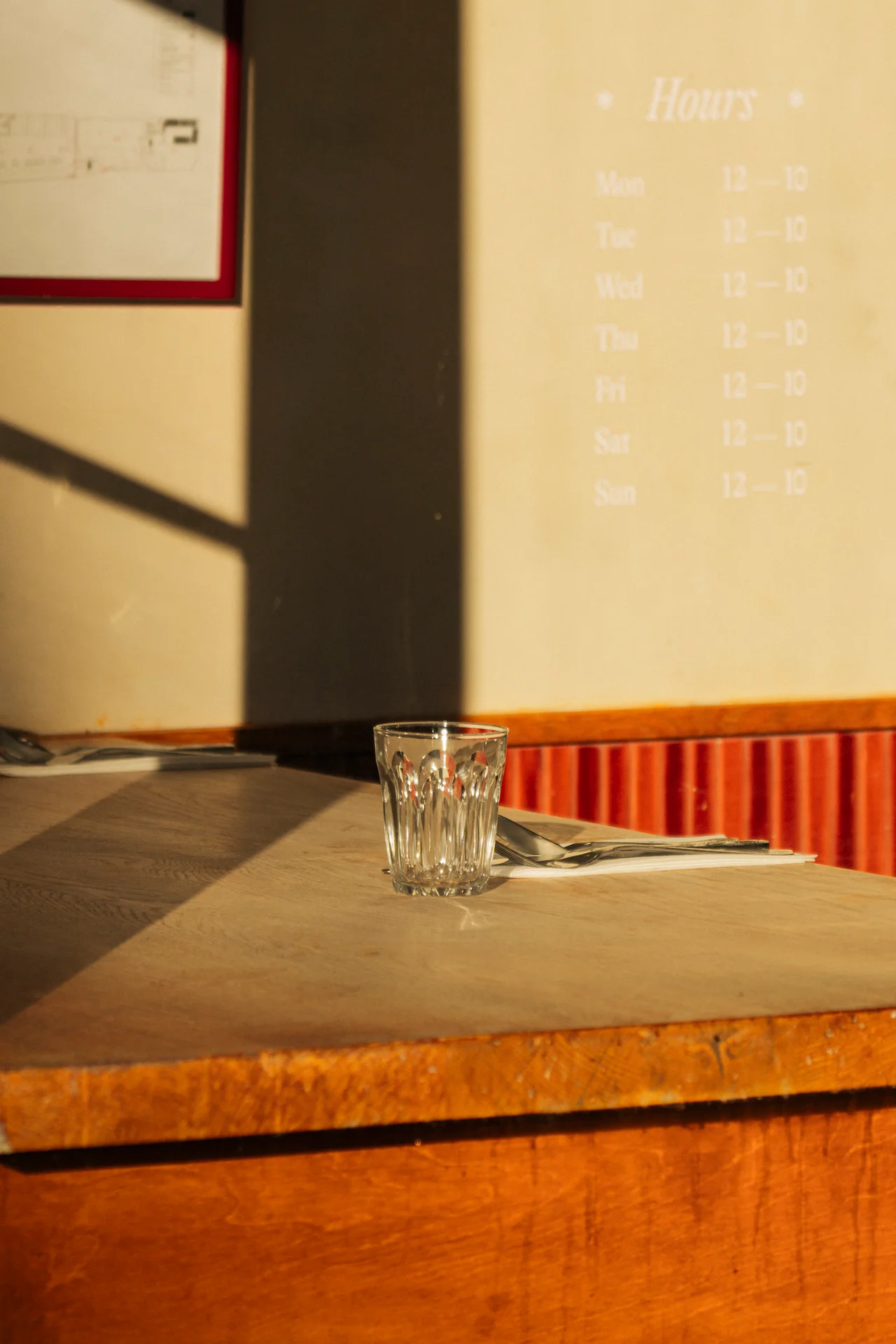 An empty glass on a table beneath the Hours board