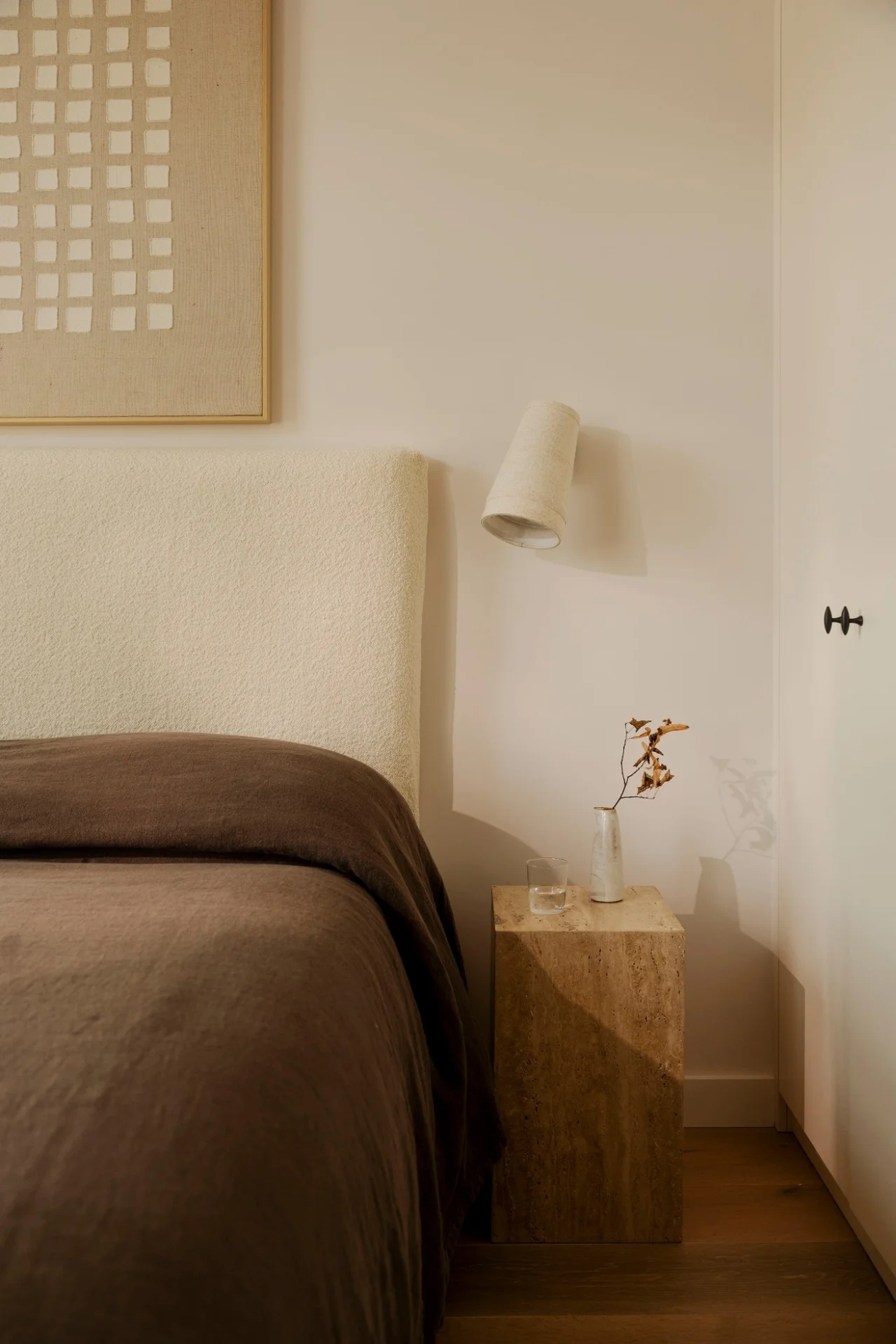 Bed with a textured headboard, wall light and travertine bedside table